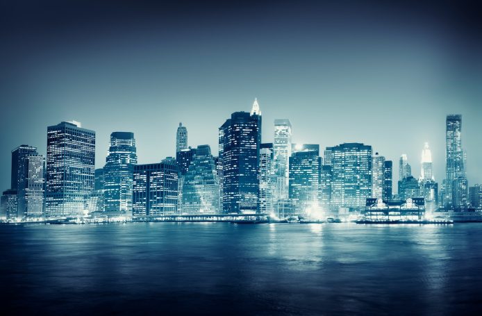 City skyline at night with illuminated buildings and a moody blue atmosphere.