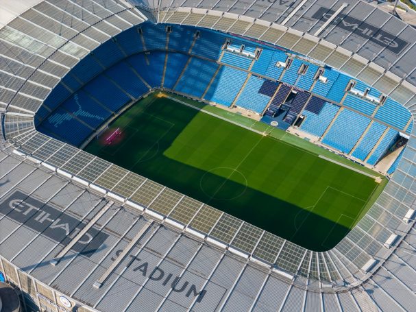 Aerial view of the Etihad Stadium with a green pitch and blue seating.